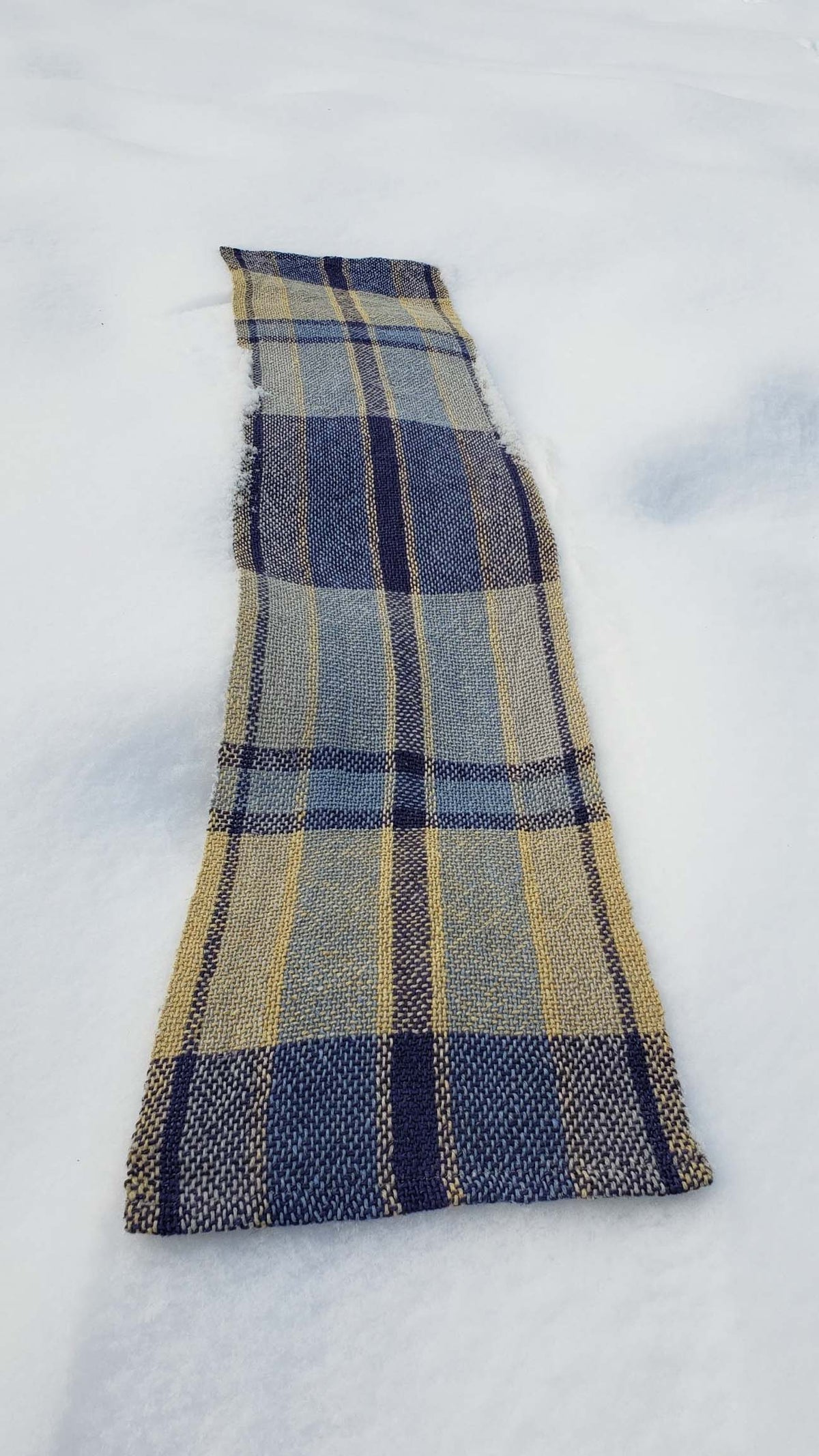 Handwoven plaid table runner on a blanket of snow.