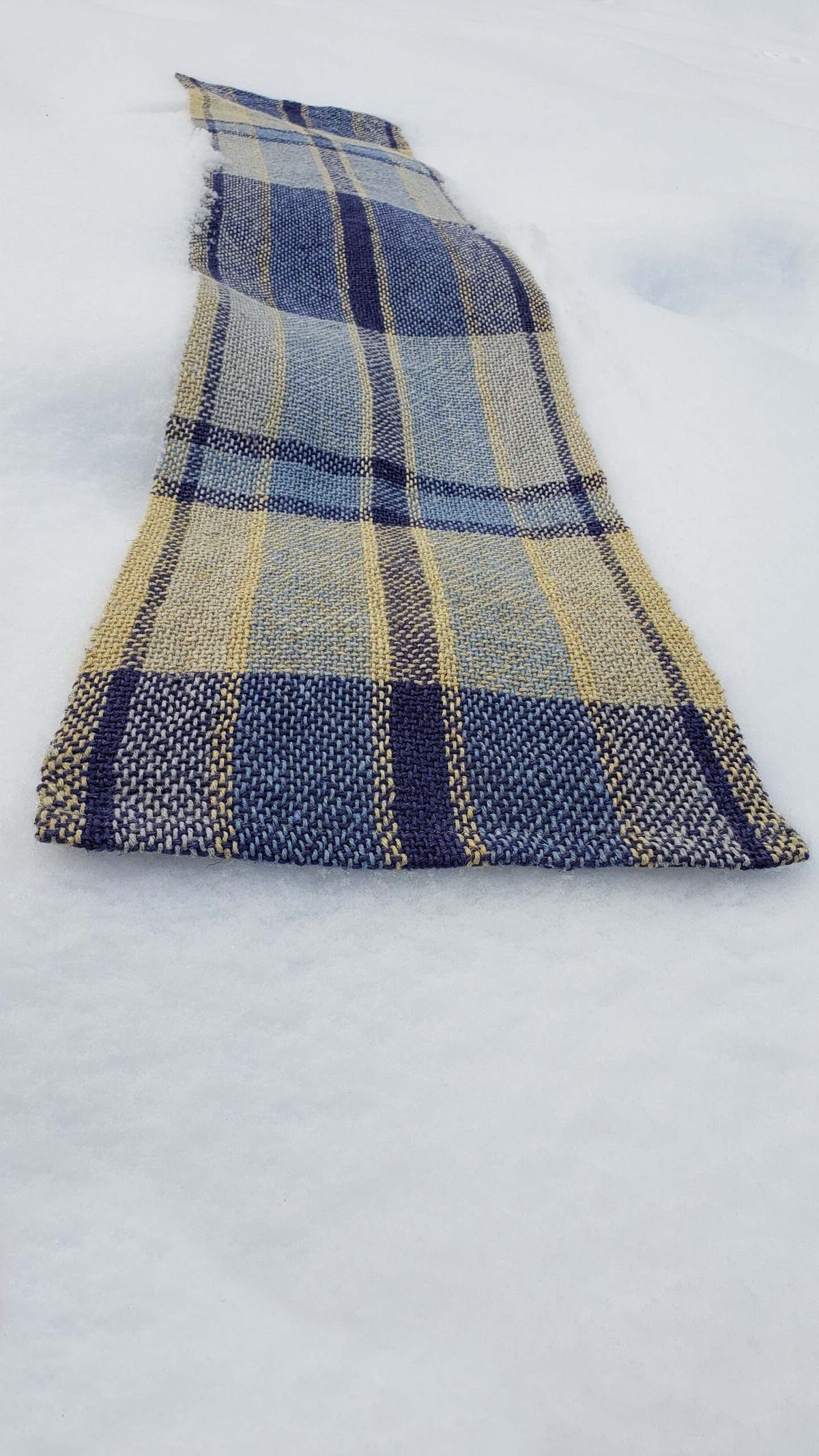 Handwoven plaid table runner on a blanket of snow.