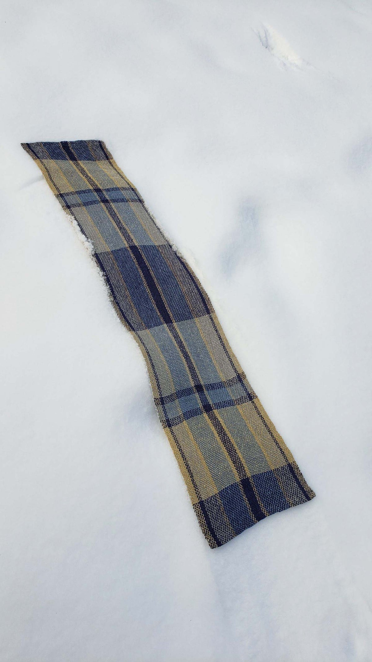 Handwoven plaid table runner on a blanket of snow.