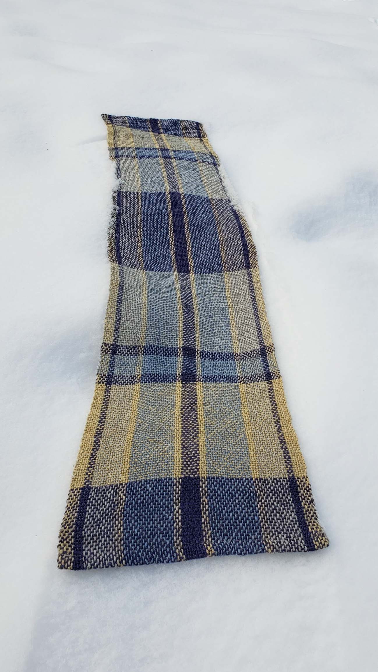 Handwoven plaid table runner on a blanket of snow.
