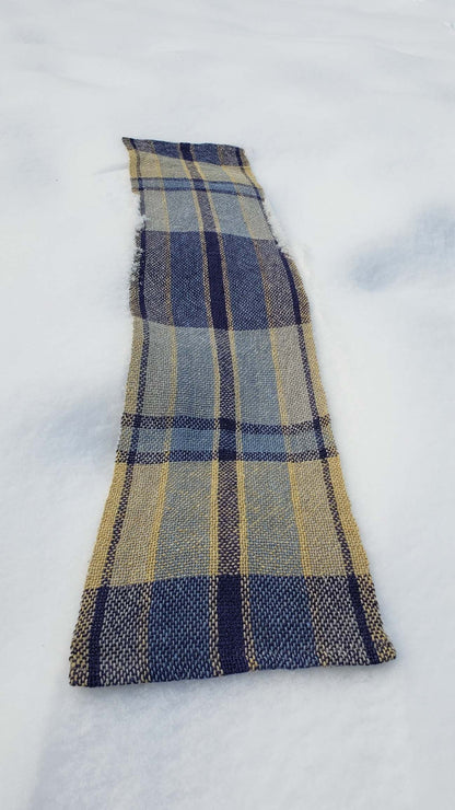 Handwoven plaid table runner on a blanket of snow.