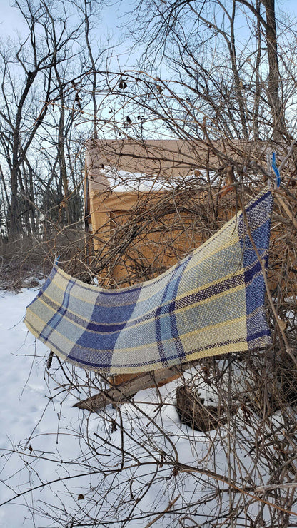 Plaid handwoven table runner draped over branches in a snowy landscape with bare trees.