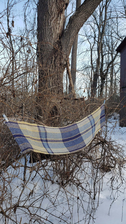 Plaid handwoven table runner draped over branches in a snowy landscape with bare trees.