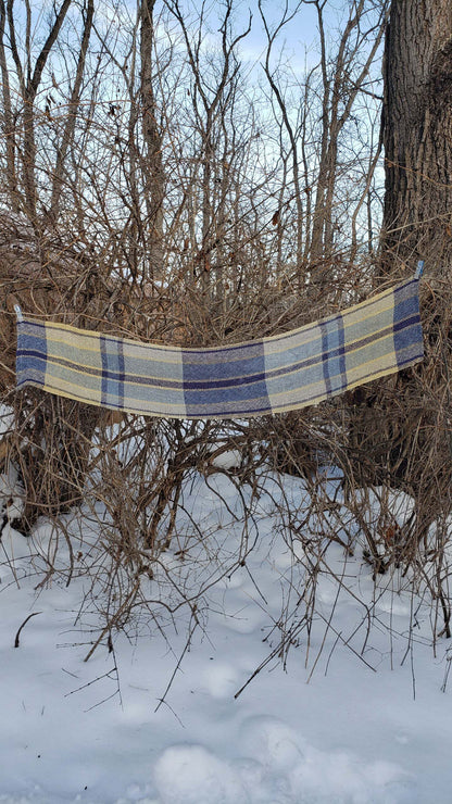 Handwoven plaid table runner draped across branches in a snowy wooded background.