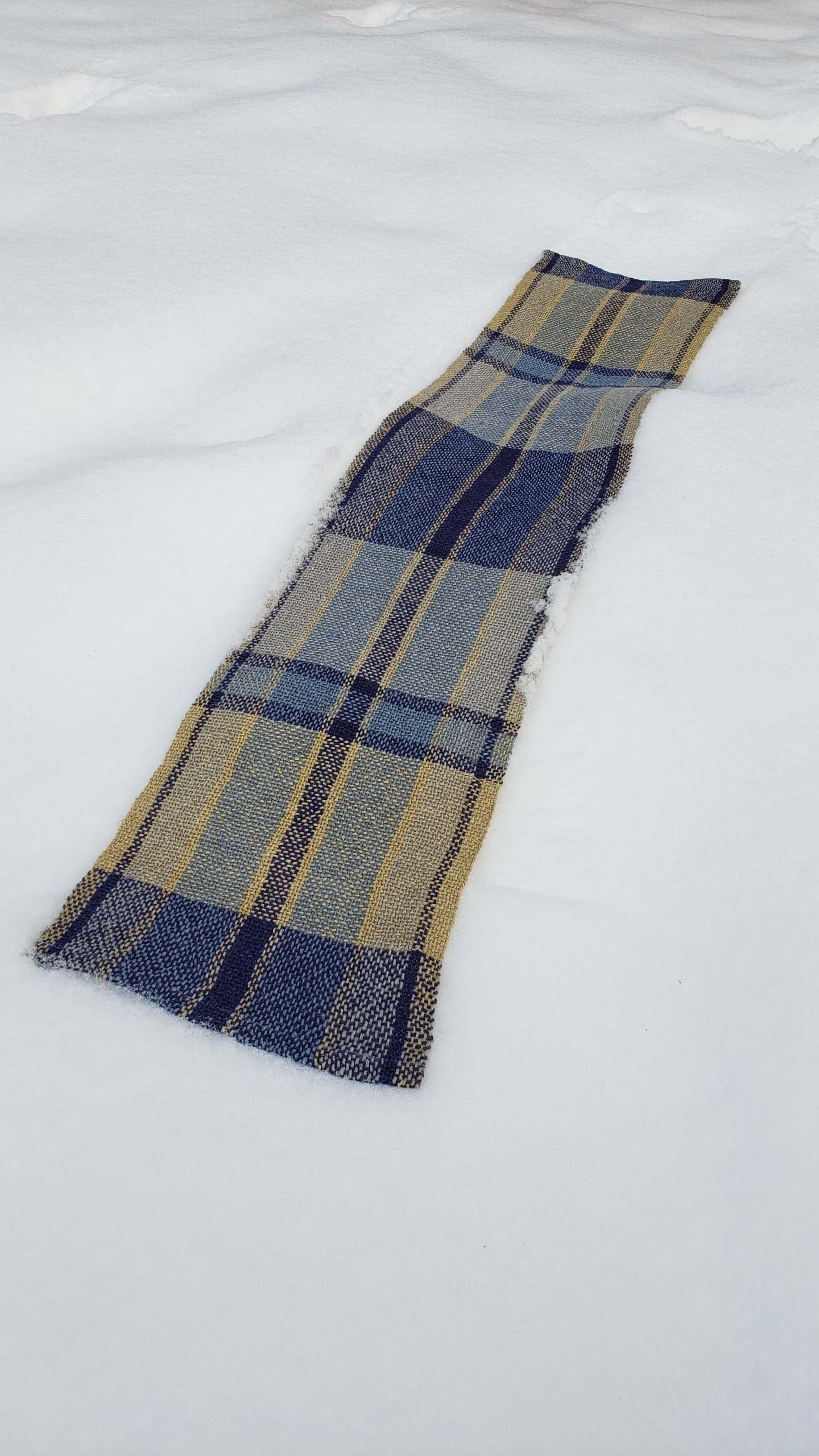 Handwoven plaid table runner on a blanket of snow.