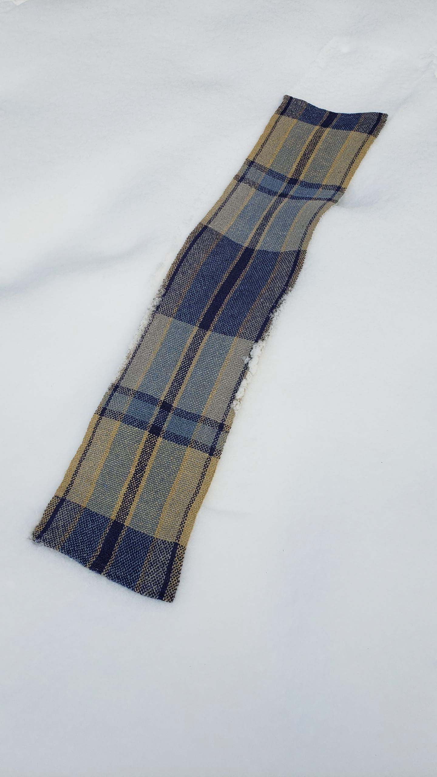 Handwoven plaid table runner on a blanket of snow.