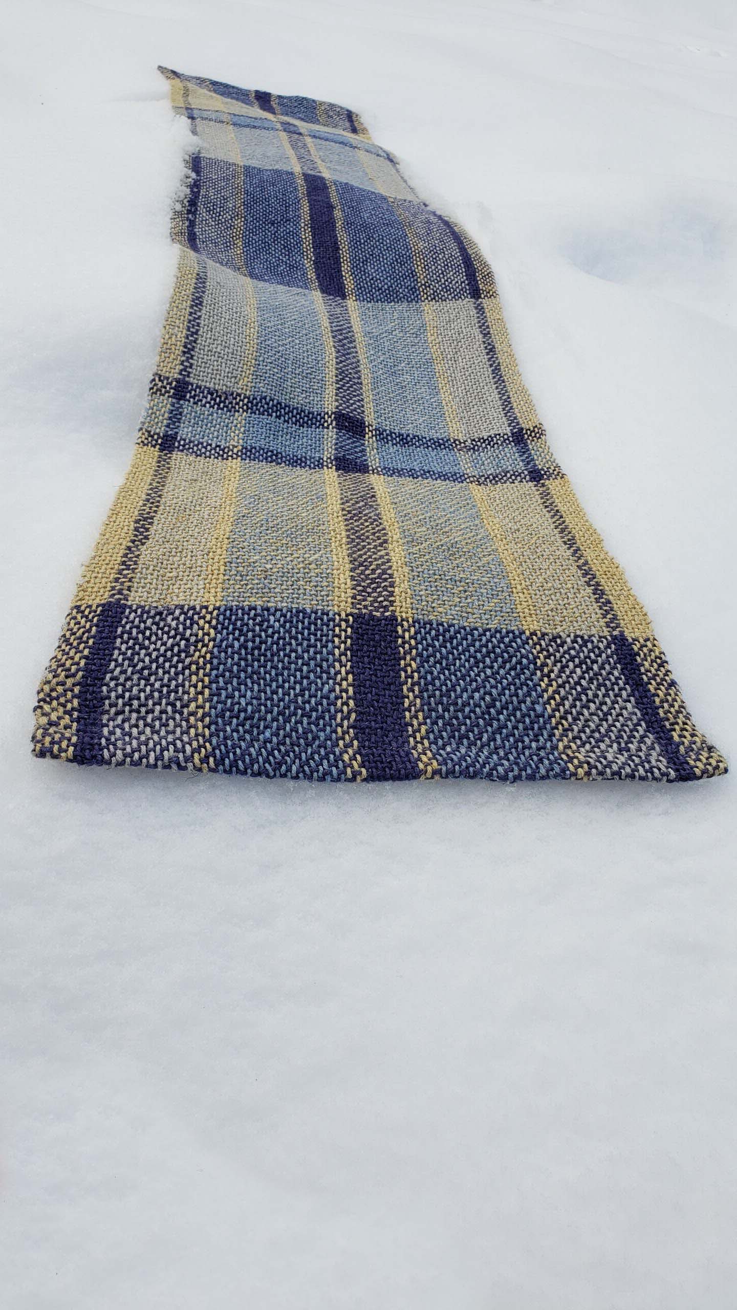 Handwoven plaid table runner on a blanket of snow.