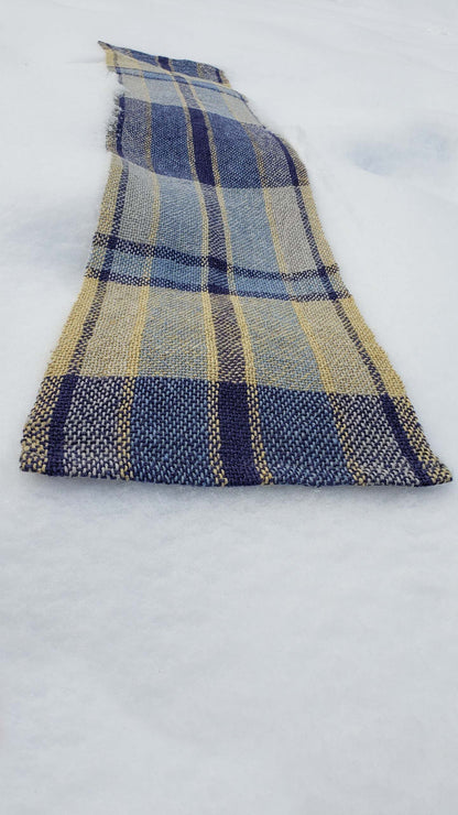 Handwoven plaid table runner on a blanket of snow.