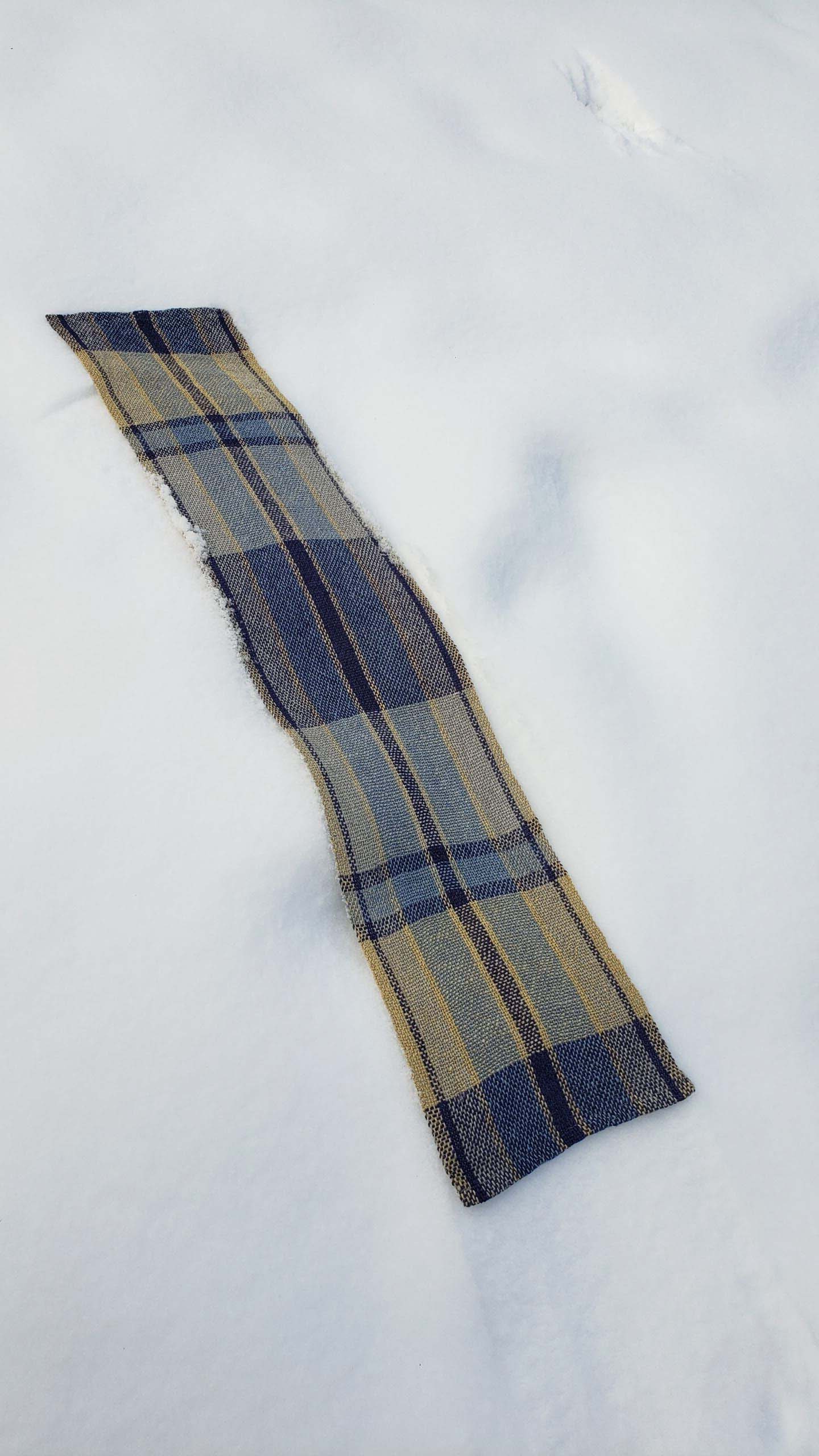 Handwoven plaid table runner on a blanket of snow.