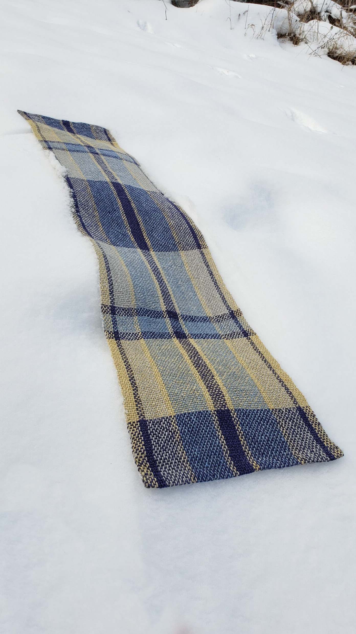 Handwoven plaid table runner on a blanket of snow.
