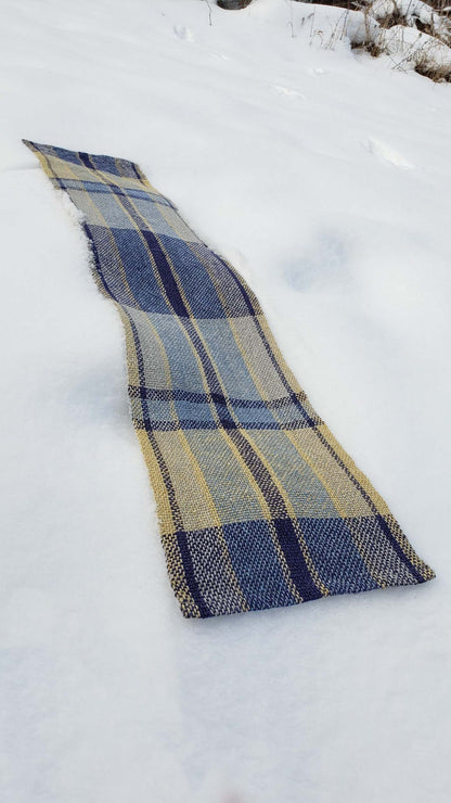 Handwoven plaid table runner on a blanket of snow.