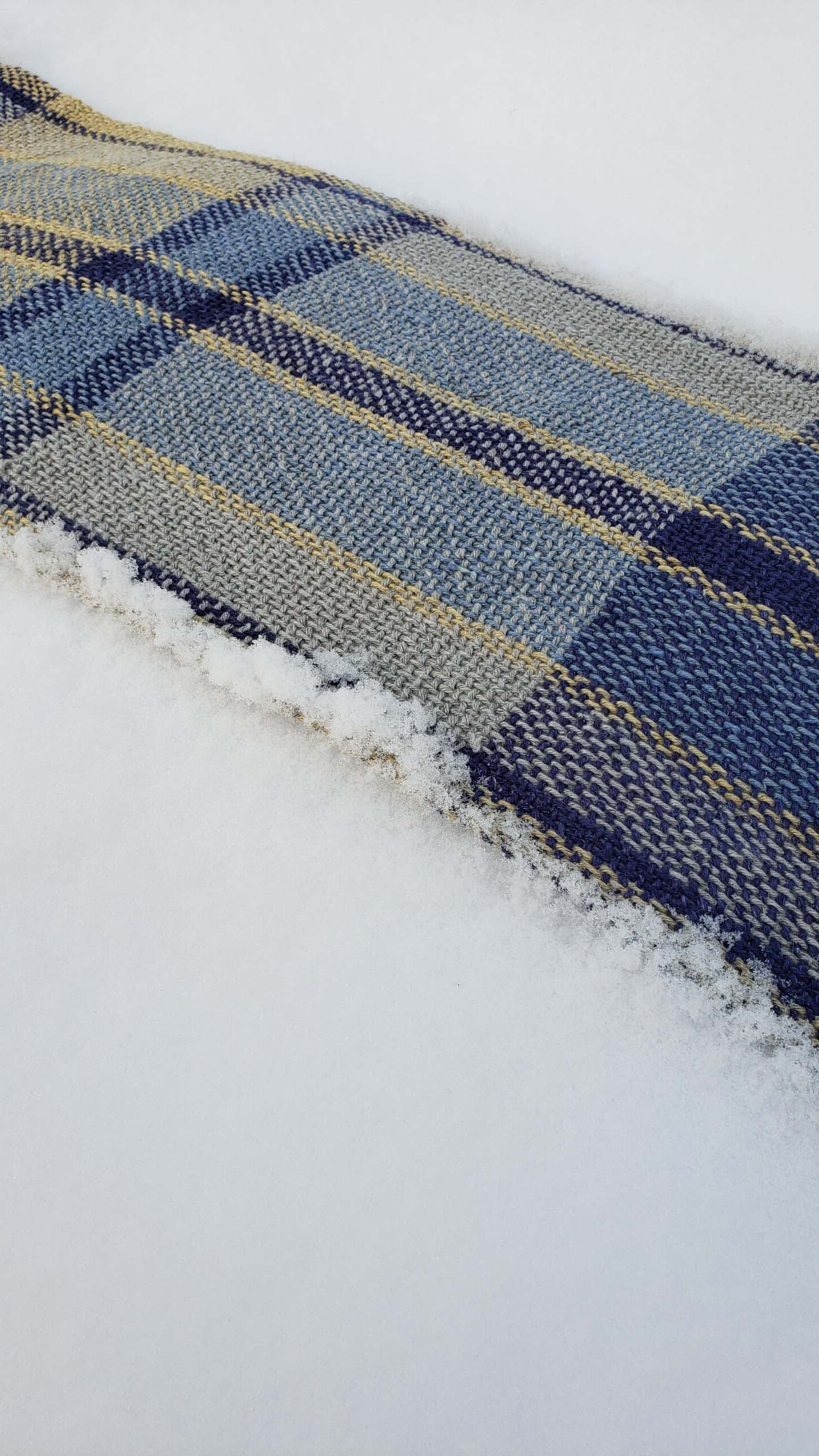 Close-up of a blue, grey and yellow plaid handwoven fabric on a snowy background